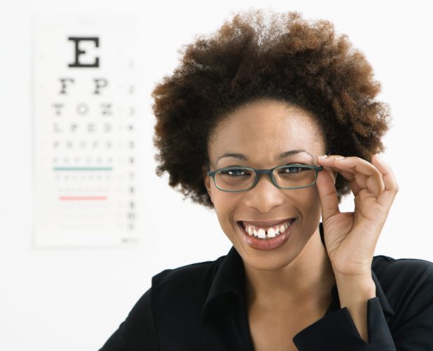 Portrait of woman with afro wearing eyeglasses with medical eyechart in background.
